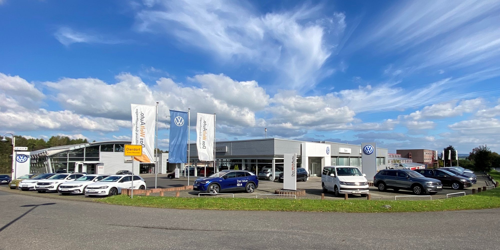 Autohaus mit mehreren Fahrzeugen vor dem Gebäude und Fahnen wehen im Vordergrund.