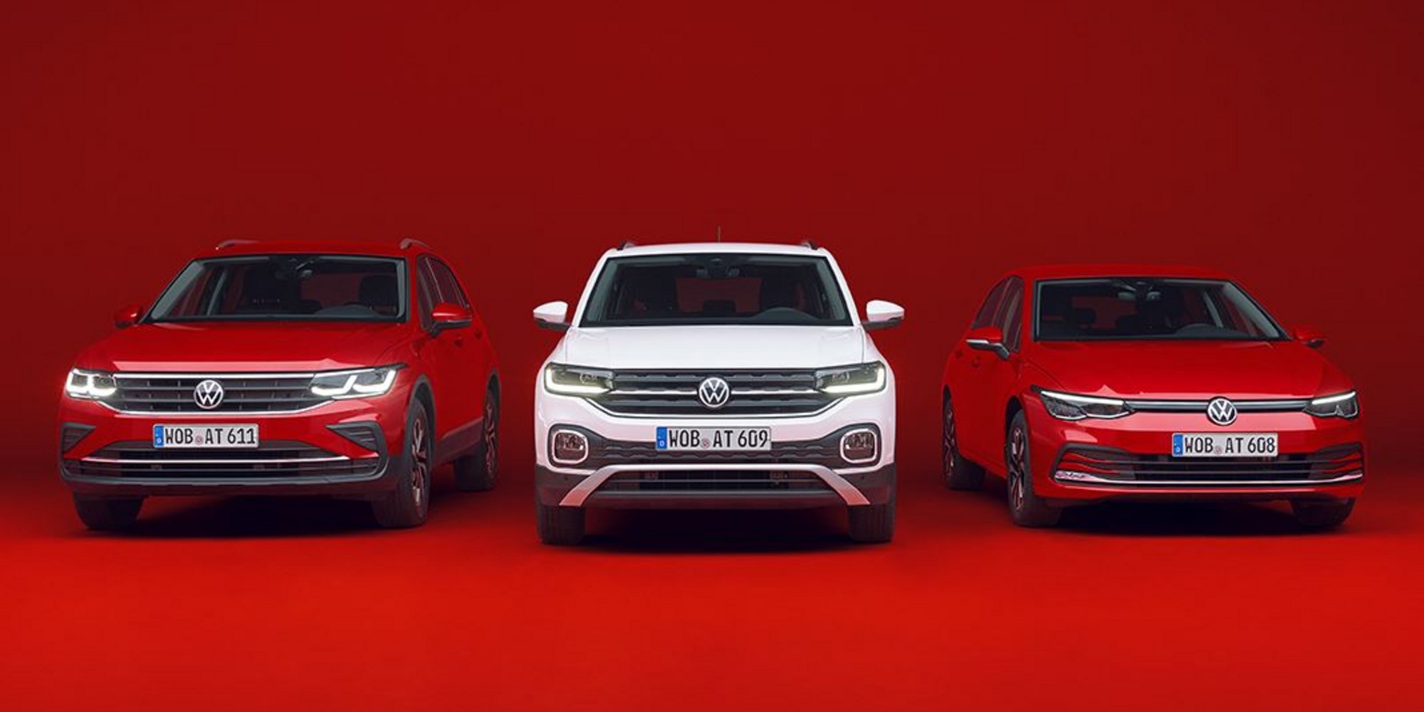 Drei Volkswagen-Fahrzeuge – zwei rote und ein weißes – stehen nebeneinander vor rotem Hintergrund.