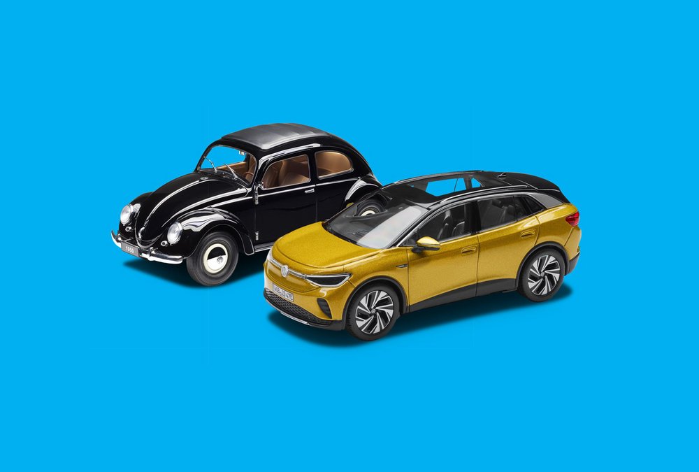 Zwei Modellautos stehen nebeneinander: ein schwarzer VW Käfer und ein goldfarbener VW ID.4 vor blauem Hintergrund.